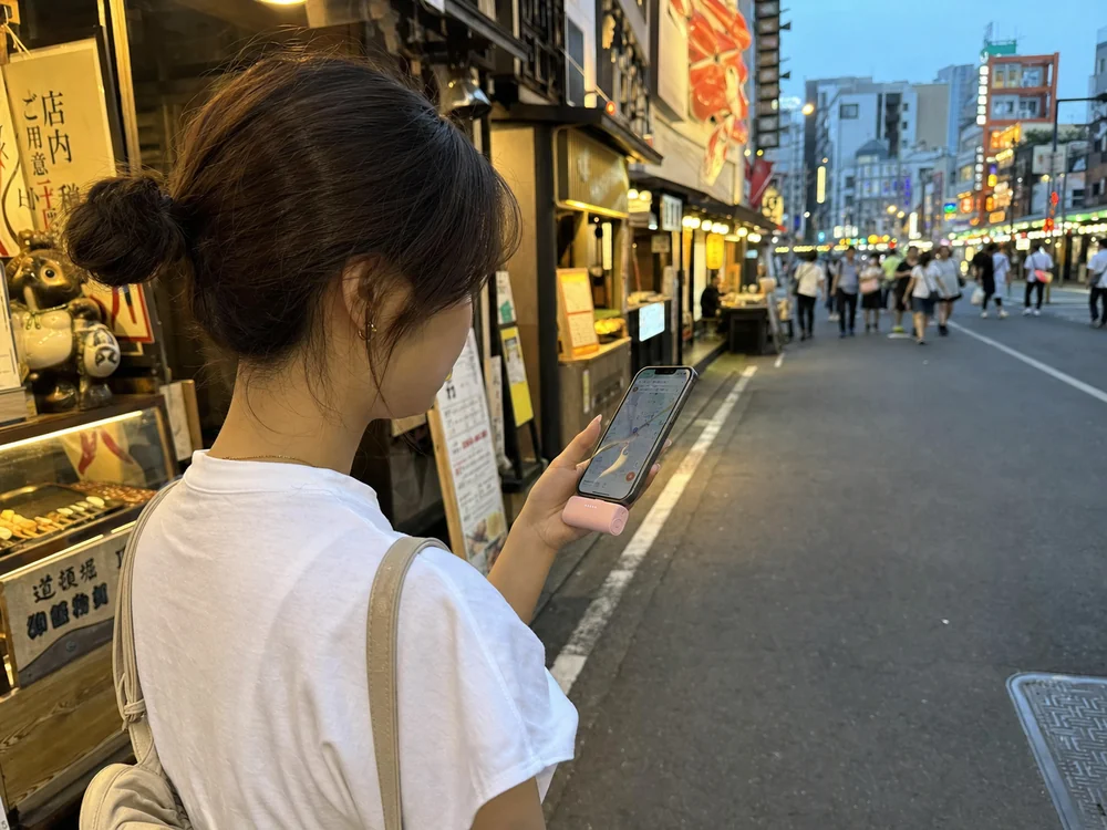 街中でiPhoneに直接つないで使うピンクの小型モバイルバッテリーのイメージ