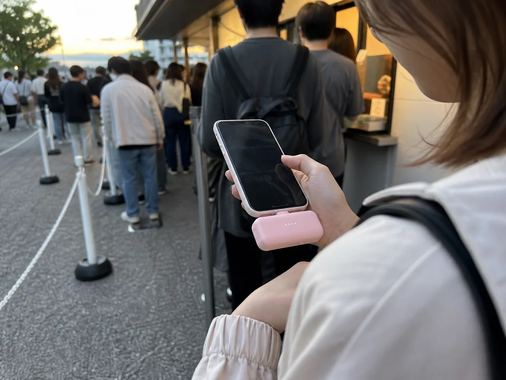 順番待ちのあいだにiPhoneへ直接つないで使うピンクの小型モバイルバッテリーのイメージ