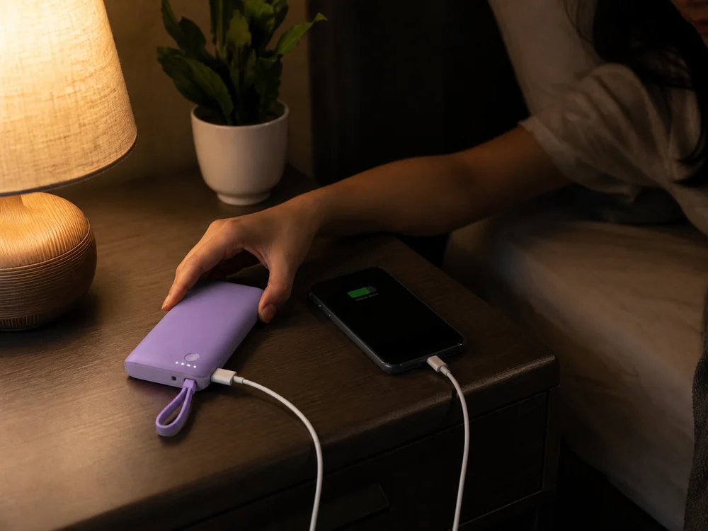 夜の室内でスマートフォンを充電する薄型パープルのモバイルバッテリー