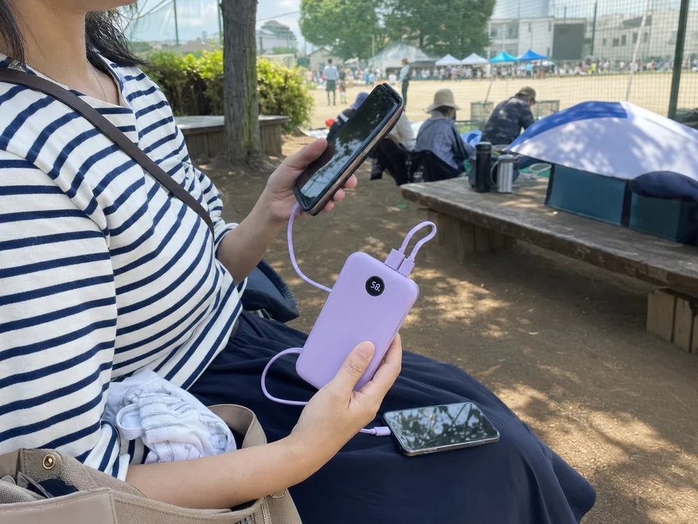内蔵ケーブル付きの紫系モバイルバッテリーで屋外イベント中にスマホを立て直す利用シーン
