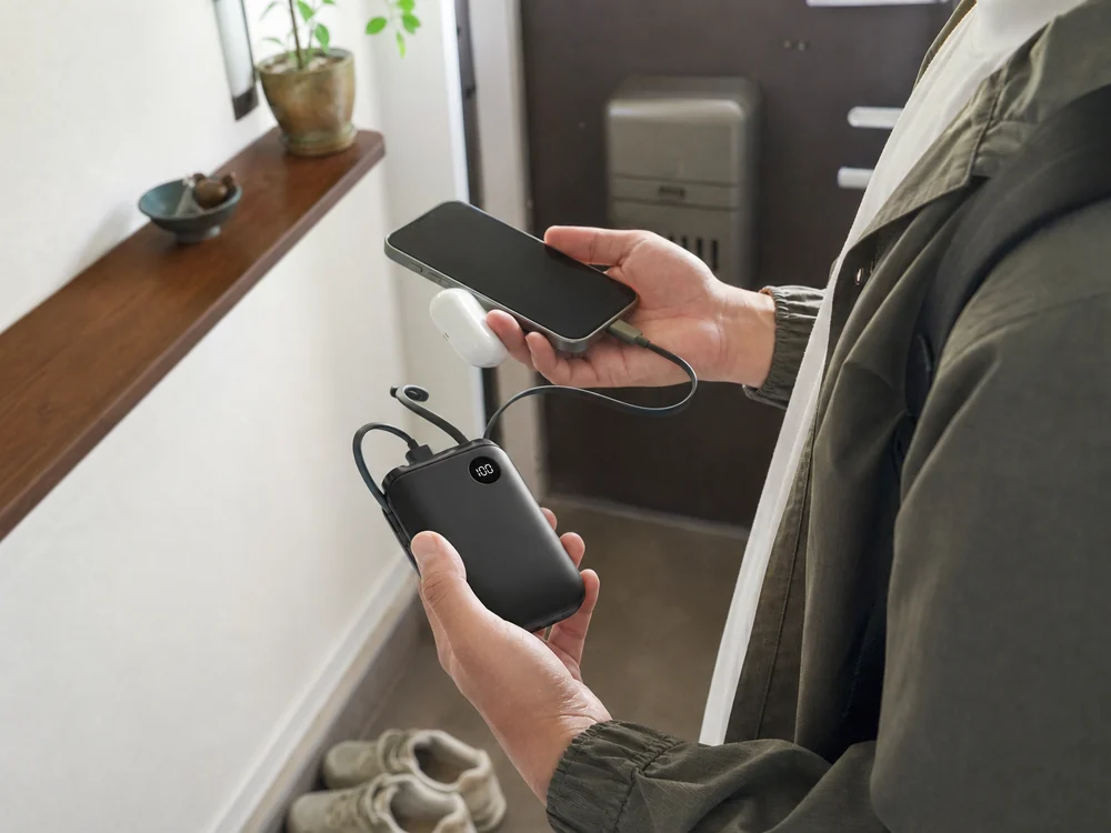 玄関前でスマホと一緒に持ち出し準備をするケーブル内蔵モバイルバッテリーの使用イメージ