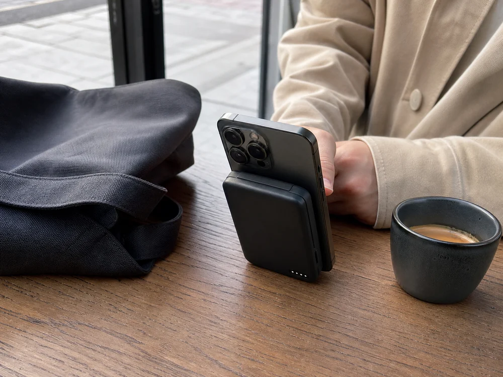 MagSafe対応の黒いモバイルバッテリーをスマートフォンに付けてカフェで使うイメージ