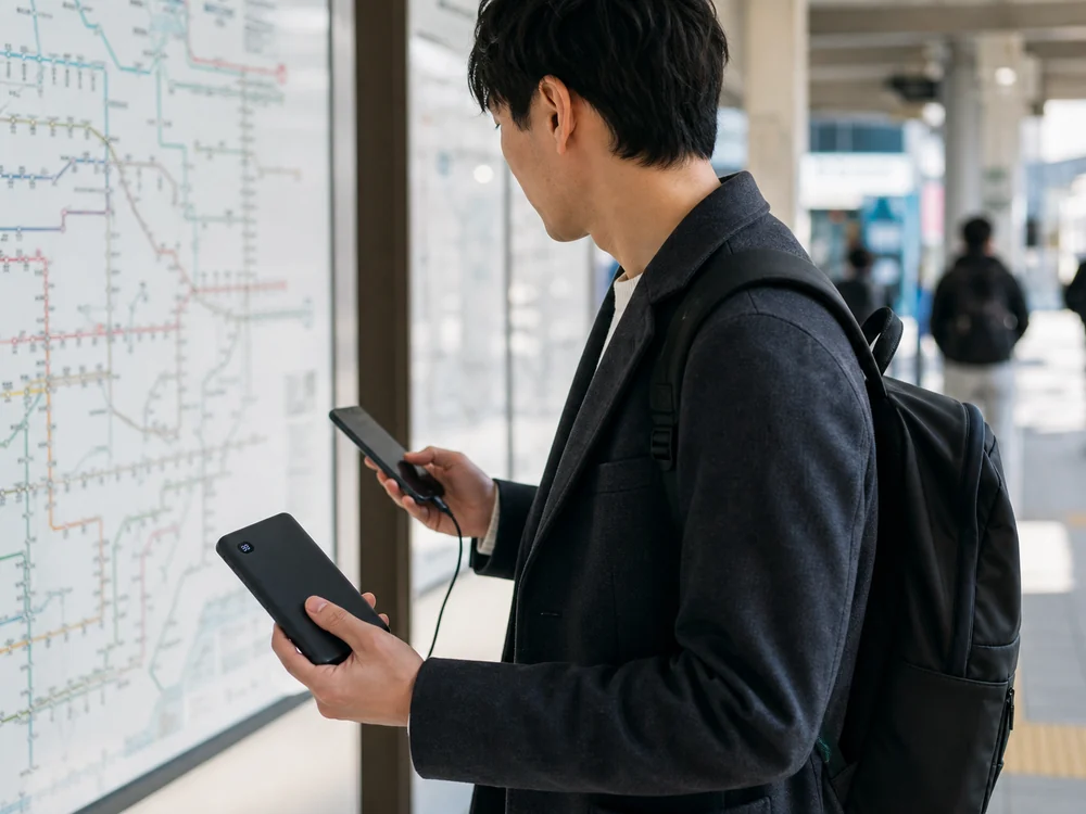 駅で路線を確認しながら薄型モバイルバッテリーでスマホを充電する様子
