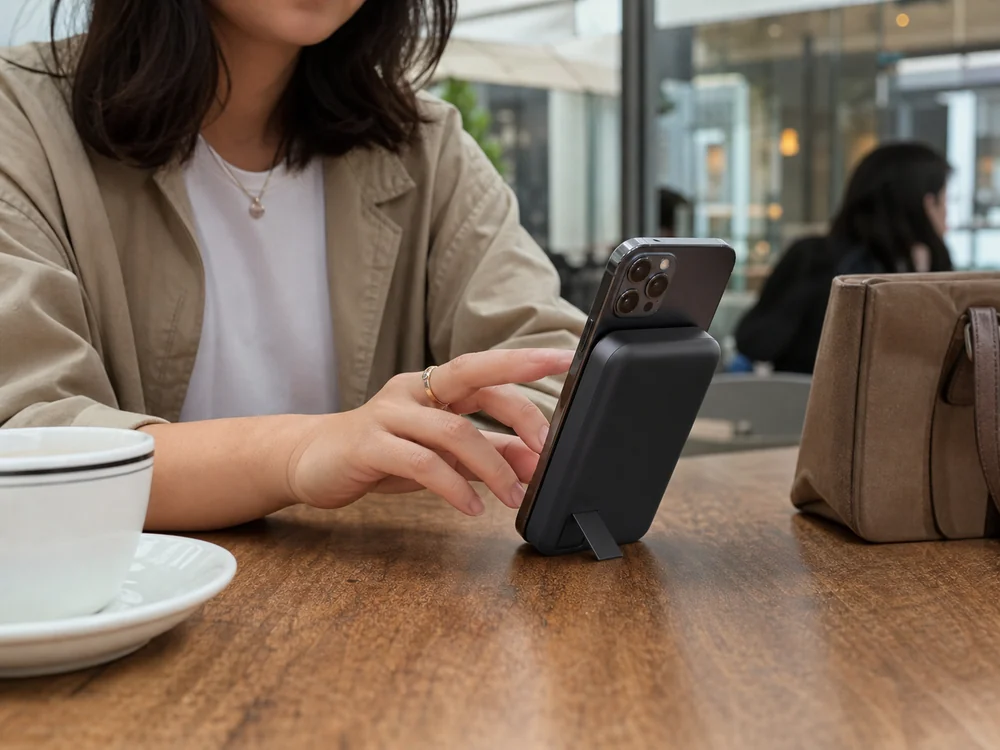 カフェのテーブルでスマホ背面に装着して使う黒いMagSafe対応モバイルバッテリー