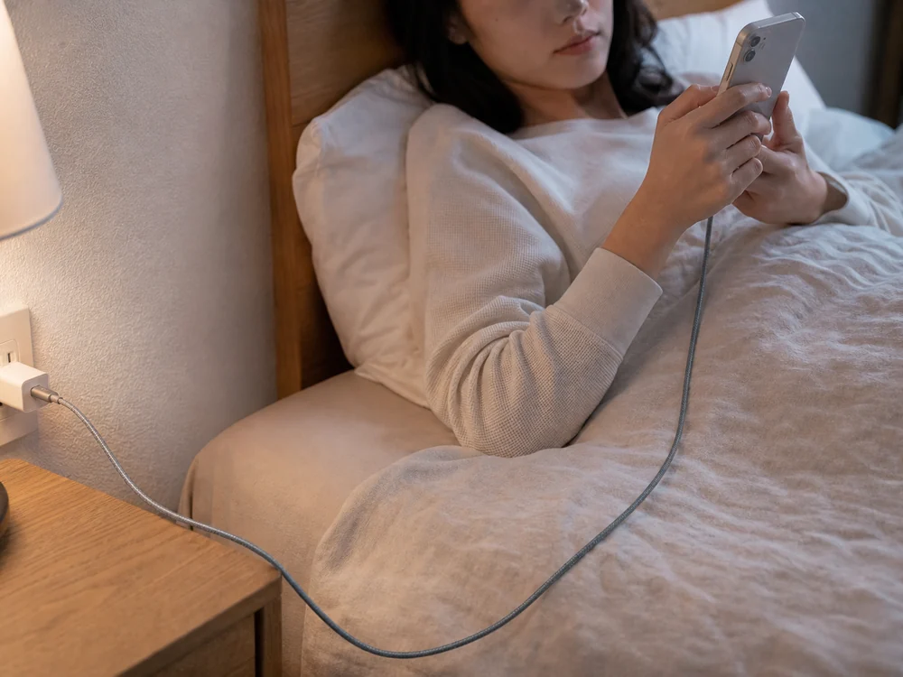 ベッドでスマホを使いながら余裕を持って届くグレーのUSB-C Lightningケーブルの使用イメージ