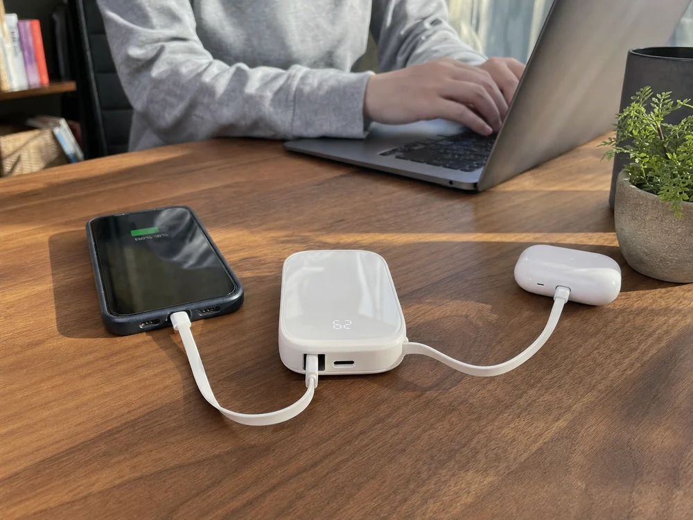 デスクでスマホとイヤホンを充電する白いモバイルバッテリーの使用イメージ