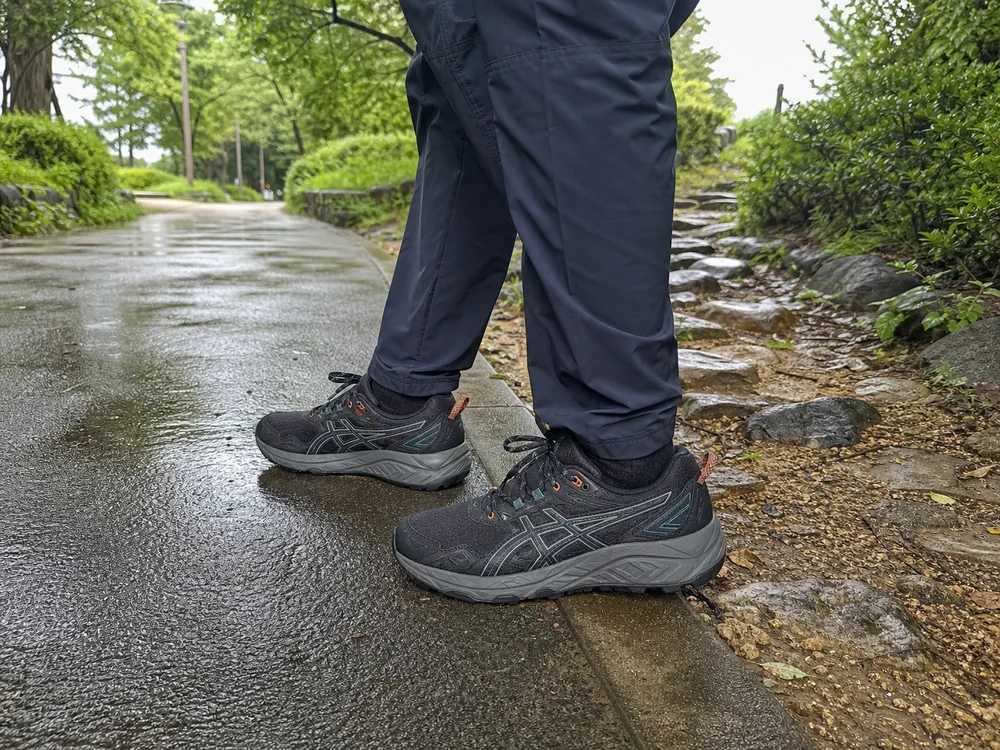 雨上がりの公園で濡れた舗装路と石混じりの道をまたいで立つGEL-VENTURE 10