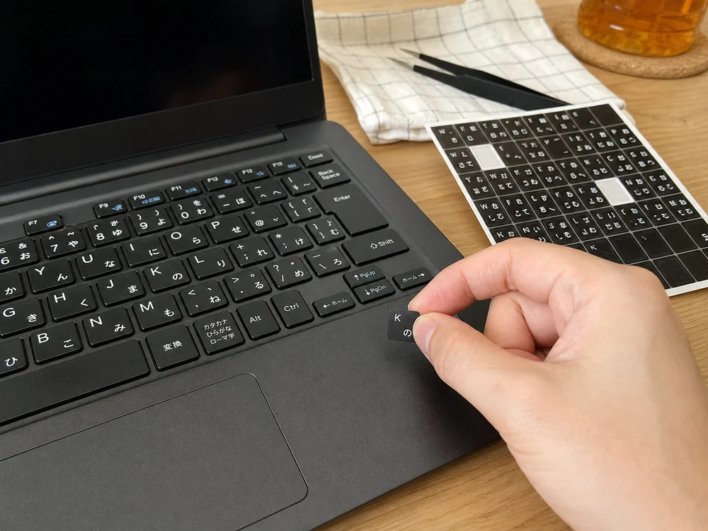 黒いノートPCのキーサイズを見ながら日本語キーボードシールを位置合わせしているシーン