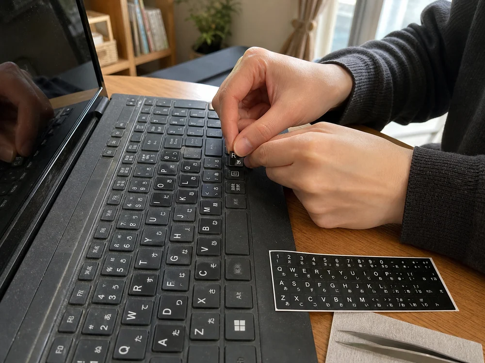 黒いノートPCキーボードに日本語シールを貼って見やすさを戻しているシーン