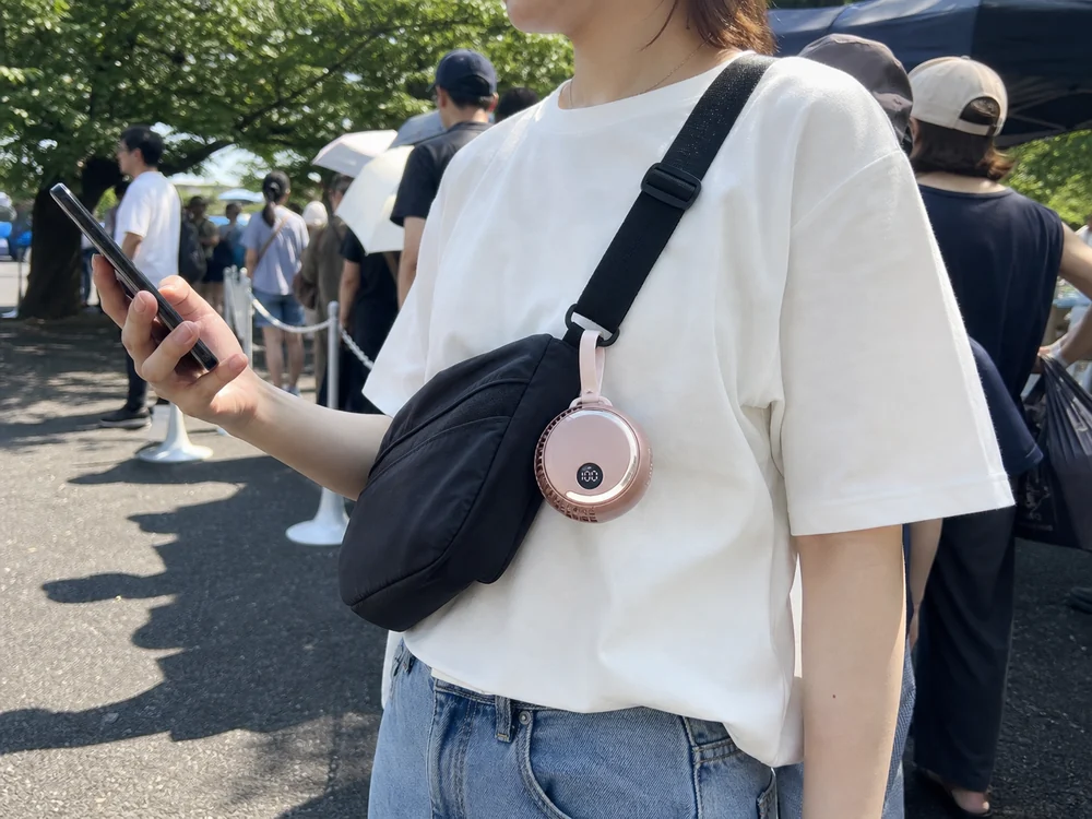 屋外イベントの待機列で、バッグに付けた丸型ファンを使う様子