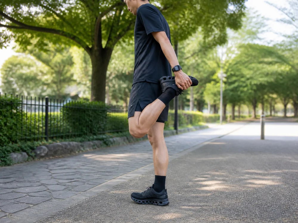 黒のCloudmonster 2で公園の遊歩道脇に立ってストレッチする男性