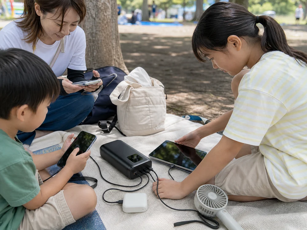 公園の休憩中に複数の端末をまとめて充電する大容量モバイルバッテリーの使用イメージ