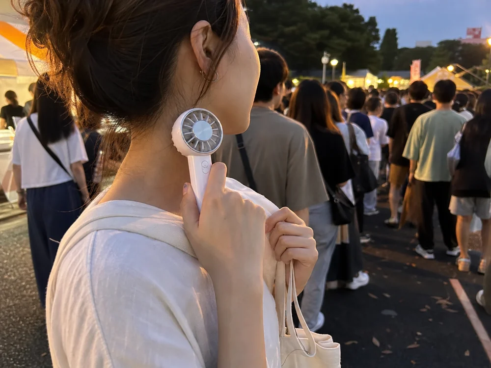 夏祭りの待機列で首元を冷やしている白い冷却プレート付きハンディファン