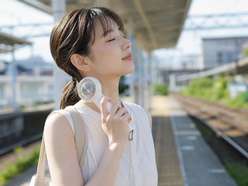 駅のホームで首元を冷やしながら使う白い冷却プレート付きハンディファン
