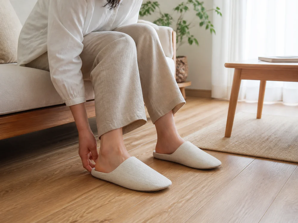 ソファ横で白系のルームシューズに足を入れる様子