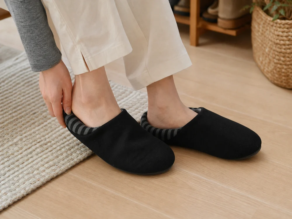 黒いバブーシュ型ルームシューズを自宅でさっと履く様子