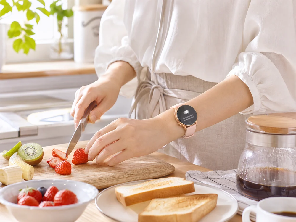 朝食を作りながらピンクの丸型スマートウォッチで通知を確認する様子