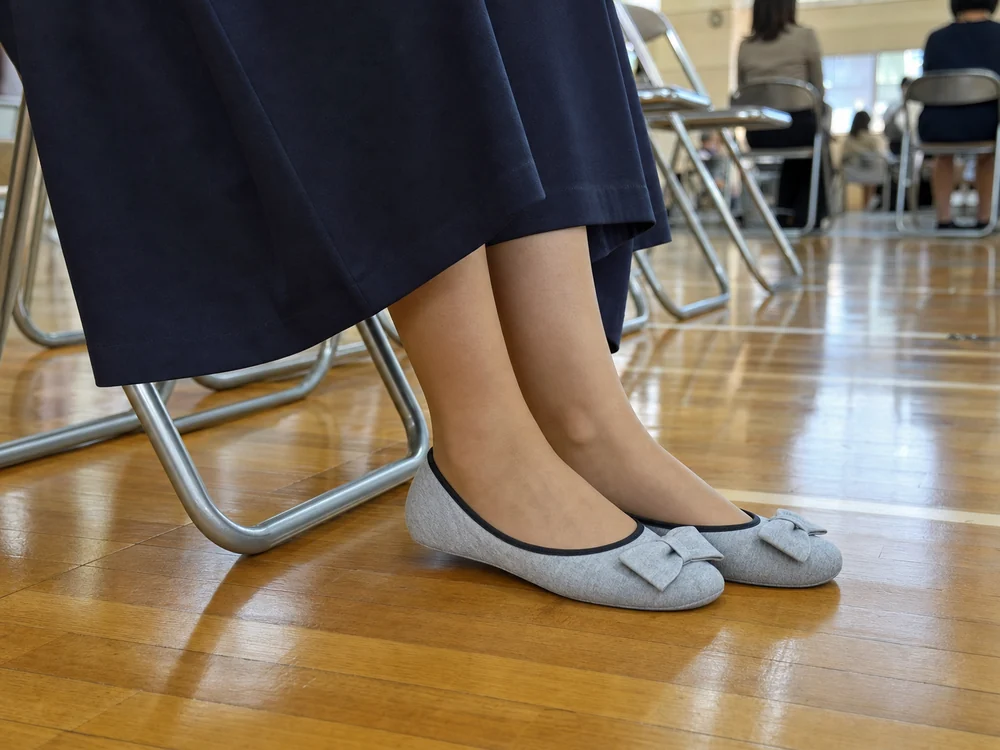 体育館の説明会でグレーのリボン付き携帯スリッパを履く保護者の足元