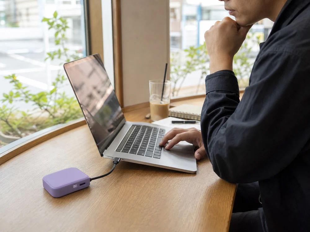カフェで紫色のモバイルバッテリーからノートPCへ給電する様子