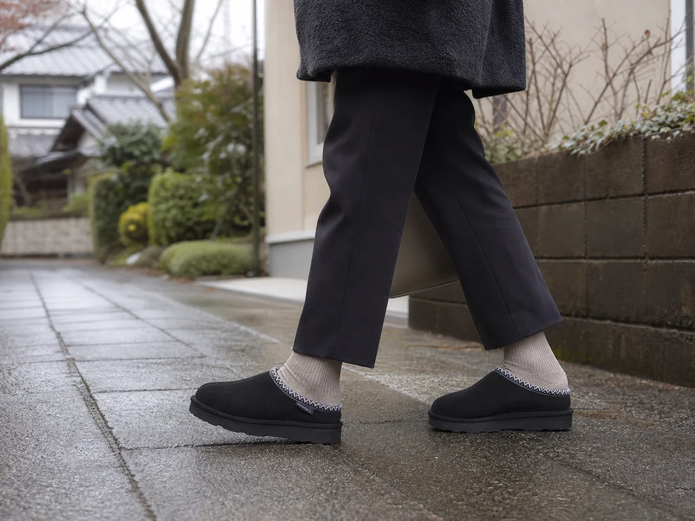 雨上がりの住宅街で黒いスエードクロッグを履いて歩く女性