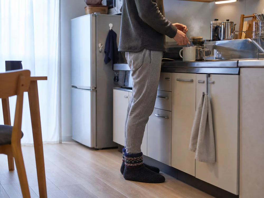 冬のキッチンで濃紺のニット製ルームシューズを履く男性
