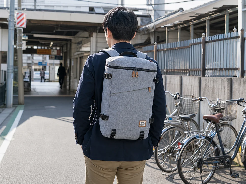 朝の駅へ向かいヘザーグレーの箱型リュックを背負う通勤者