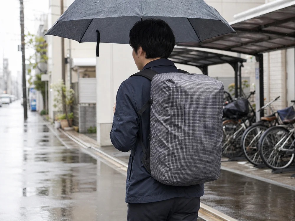 小雨の通学路でレインカバーを装着した箱型リュックを背負う人