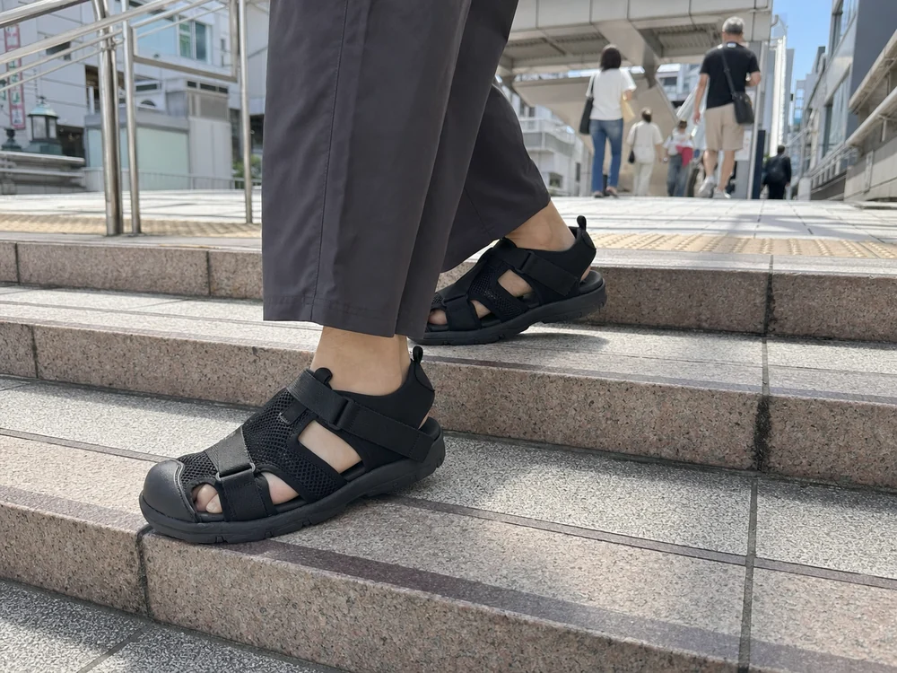 夏の街の階段を黒いサンダルスニーカーで歩く足元