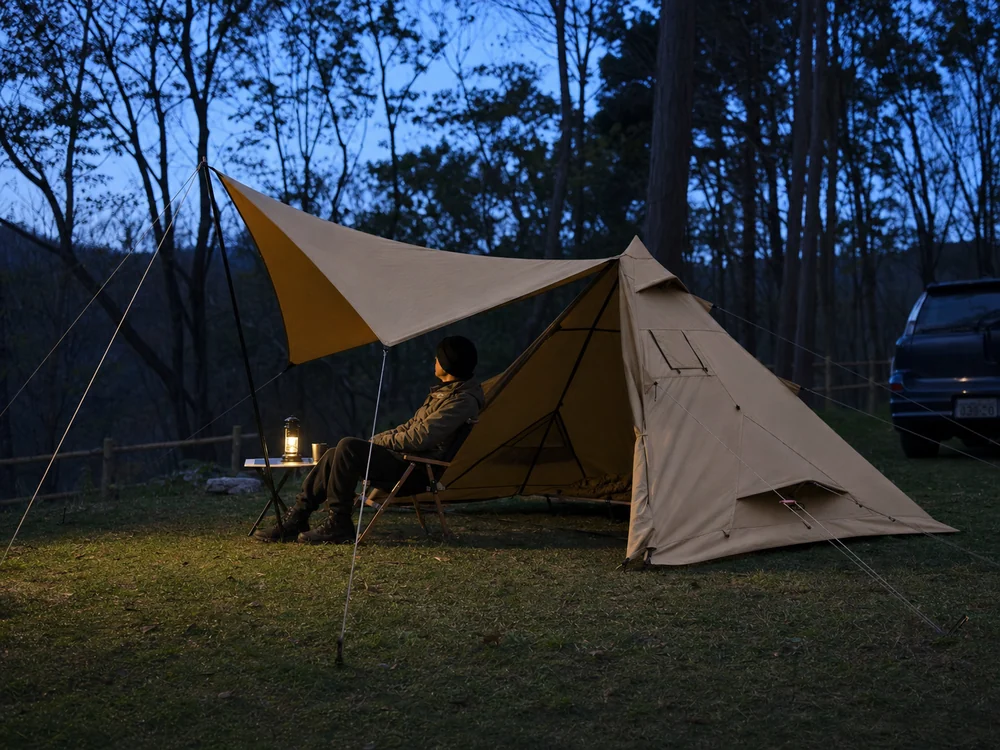 前幕のあるカーキ色のティピーテントで静かな夜を過ごすソロキャンプの風景