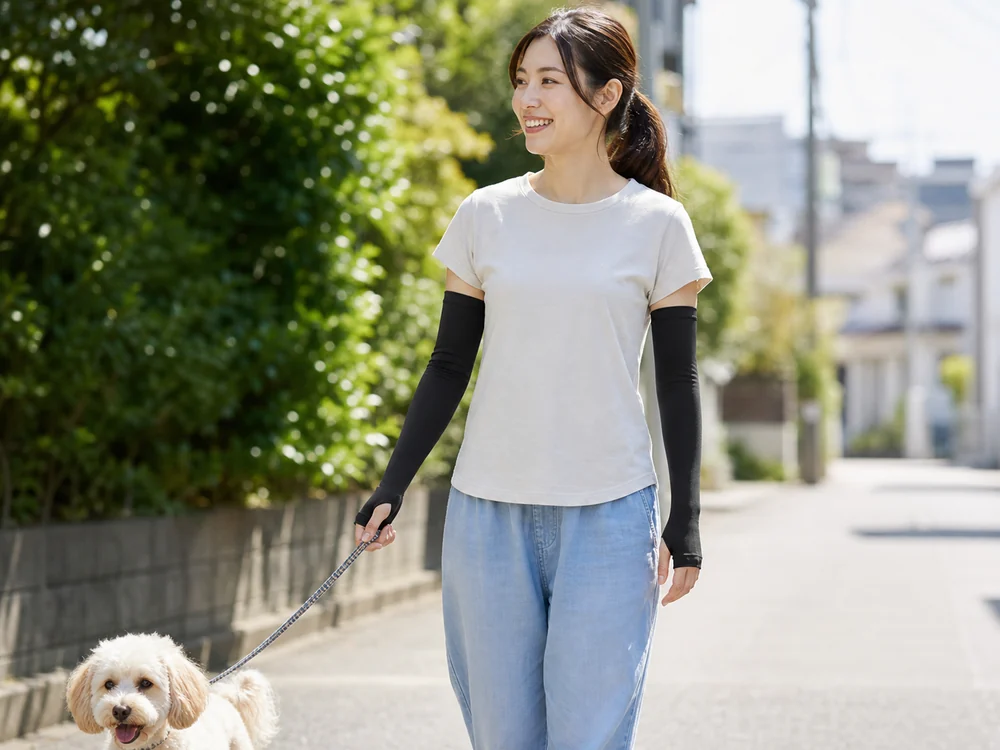 黒い冷感アームカバーを着けて夏の住宅街で犬を散歩する女性