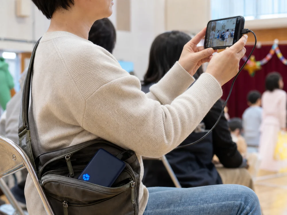 外出先で薄型の青いモバイルバッテリーを小さなバッグに入れてスマホを使う様子
