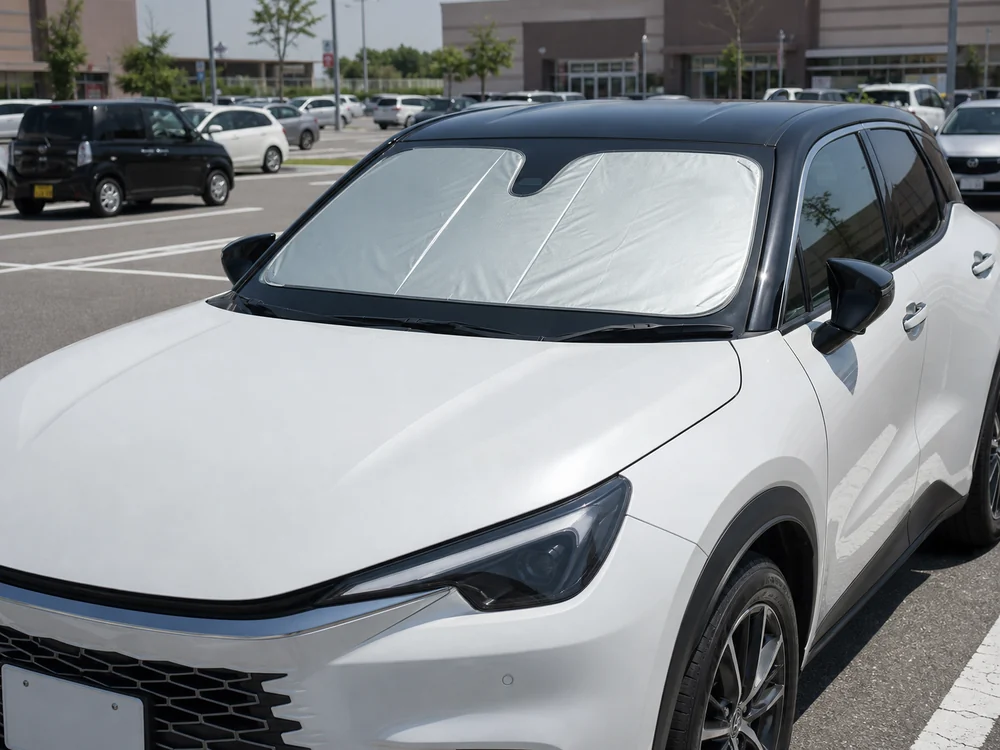 真夏の駐車場でフロントガラスに銀色の専用サンシェードを設置したコンパクトSUV
