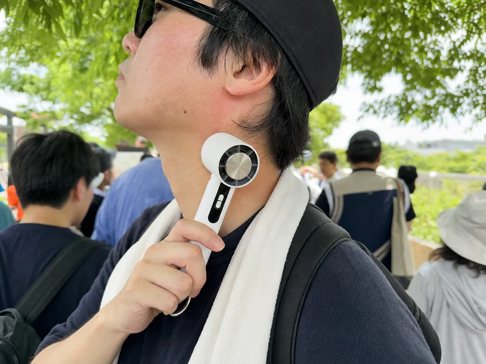 屋外イベントの待ち時間に冷却プレート付きハンディファンを首筋へ当てる様子
