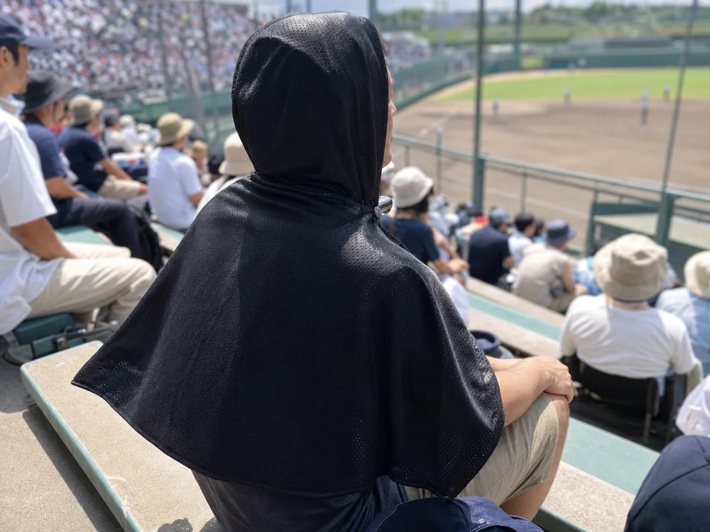 夏の屋外観戦で黒い冷感ポンチョを頭から背中まで羽織る人