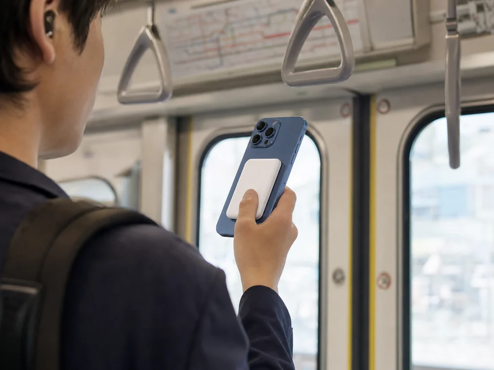 通勤電車内で白い磁気式モバイルバッテリーを付けたiPhoneを片手で持つ様子