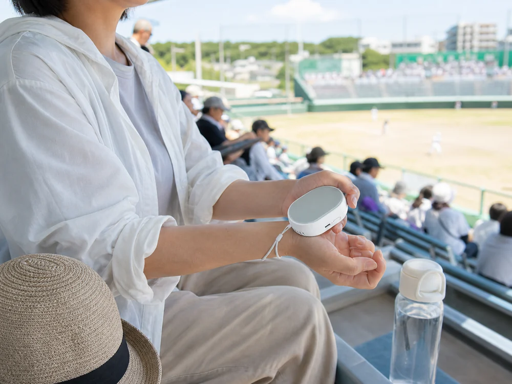 屋外スポーツ観戦で冷却プレートを手首へ当てようとする様子