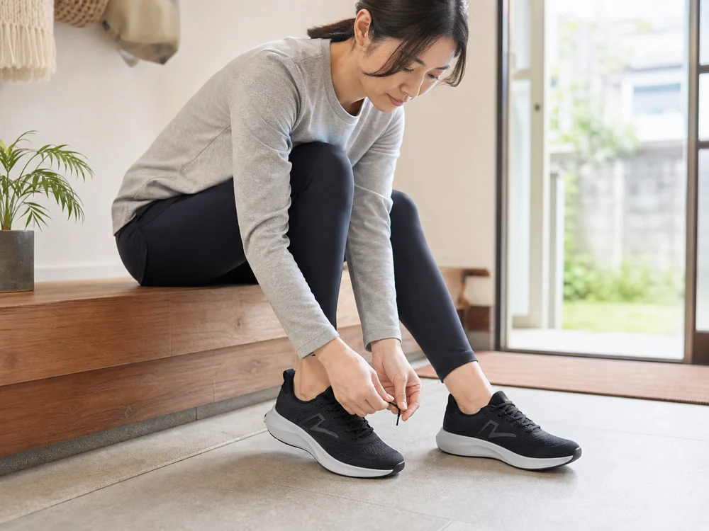 玄関のベンチで黒いメッシュスニーカーのひもを結ぶ女性