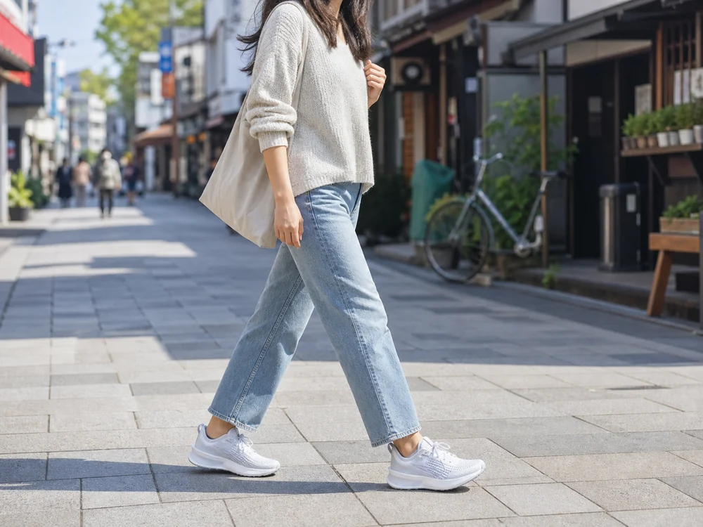 商店街を歩く女性の足元で白いランニングシューズを履いた様子
