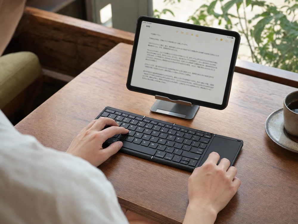 カフェの小さなテーブルでタブレットと折りたたみキーボードを使って文章を入力する様子
