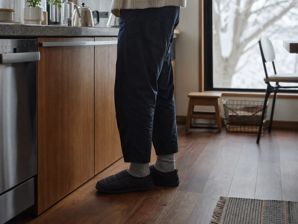 冬の朝のキッチンで黒い中綿ルームシューズを履く足元