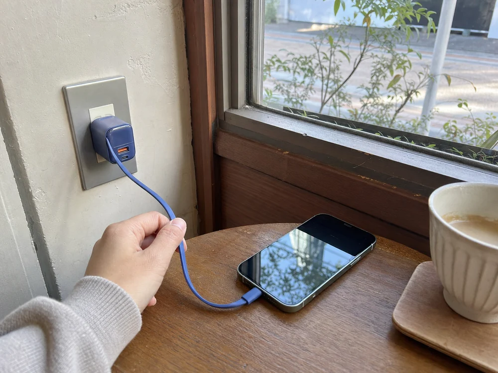 カフェの壁コンセントで青い巻き取り式充電器の内蔵USB-Cケーブルをスマートフォンにつなぐ様子