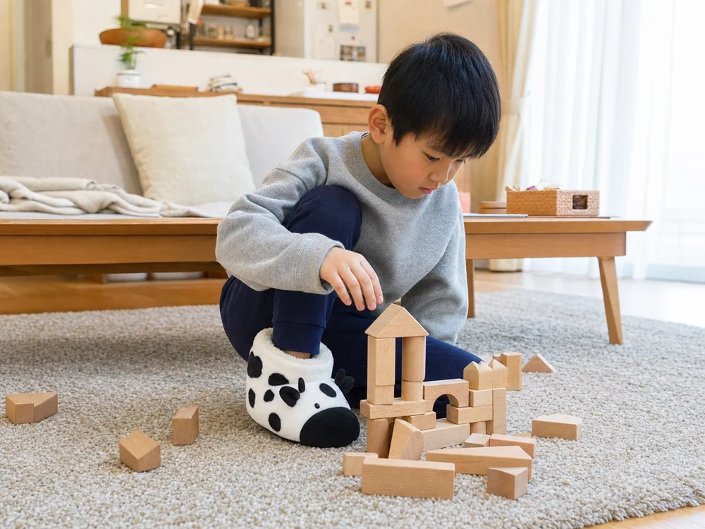 リビングで牛柄ルームシューズを履いて積み木遊びをする子ども