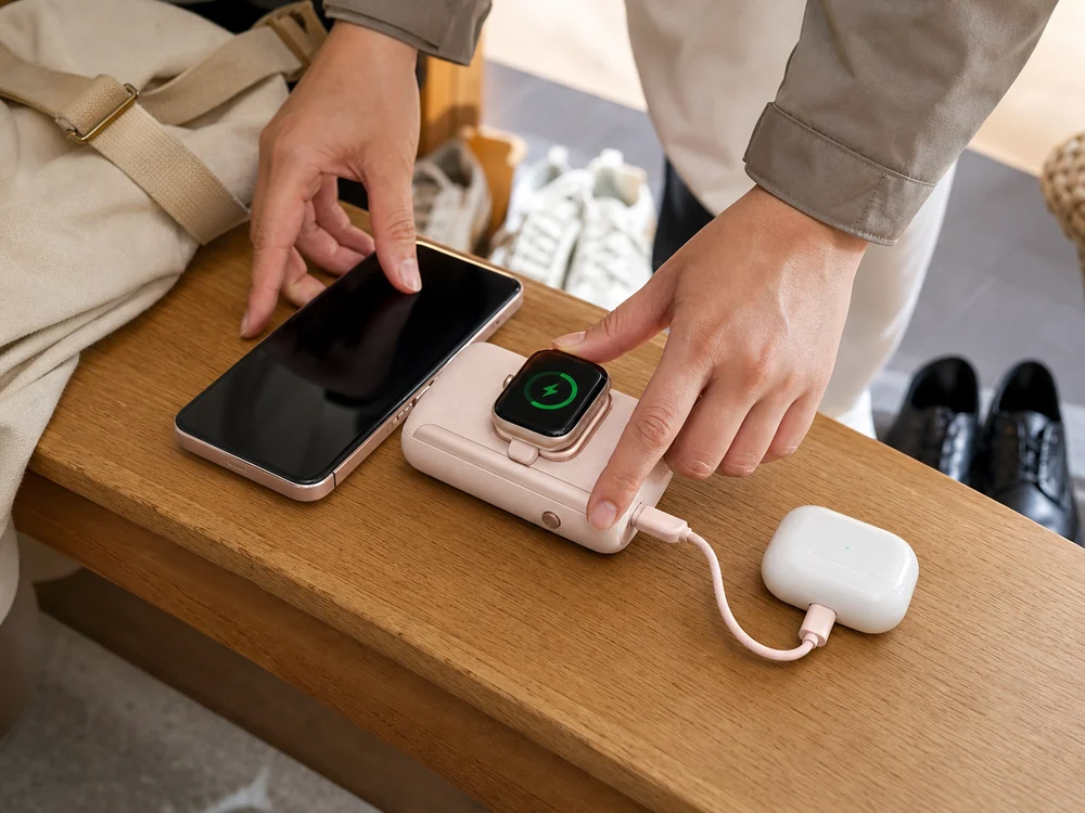 玄関ベンチで淡いピンクのモバイルバッテリーにApple Watchとイヤホンケースをつなぎ、スマホを準備する様子