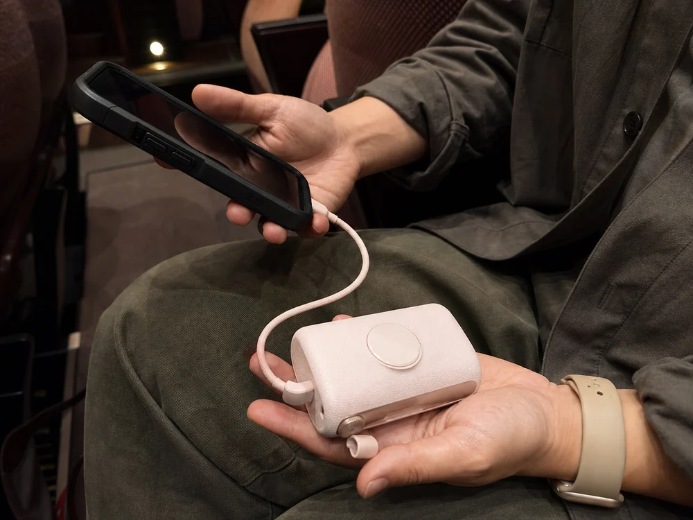 会場の座席で厚いケースのスマホを短いケーブルで淡いピンクのモバイルバッテリーにつなぐ様子