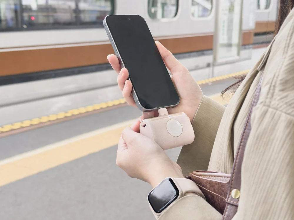 駅のホームでUSB-Cスマホに直挿しした淡いピンクのモバイルバッテリーを手で支える様子