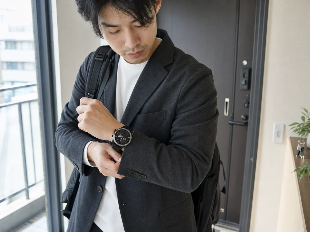 通勤前にジャケットの袖口で丸型スマートウォッチを確認する男性