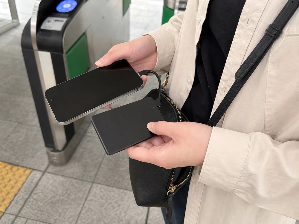 薄いモバイルバッテリーをミニバッグから取り出してスマホにつなぐ様子