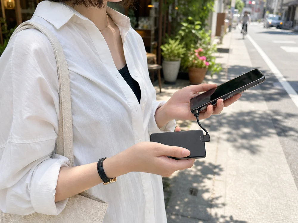 外出先で地図を見ながら薄型モバイルバッテリーでスマホを継ぎ足し充電する様子