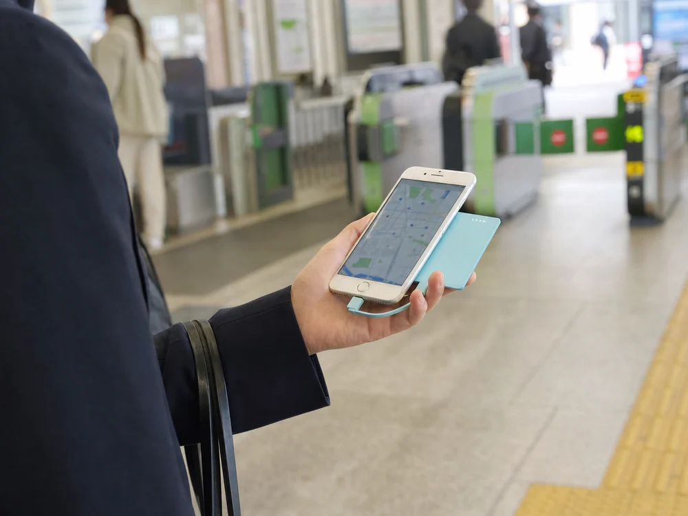 駅の改札前で水色の薄型バッテリーをLightning接続し地図を見る様子