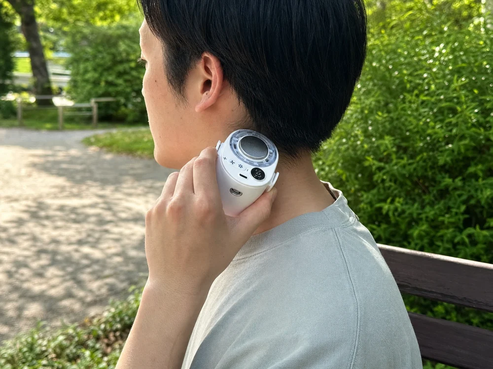白い腰掛けファンの円形冷却プレートを首筋に当てて涼む様子